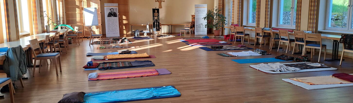 Ein großer Raum mit Parkettboden. Mehrere Gymnastikmatten mit Decken liegen verteilt im Raum.